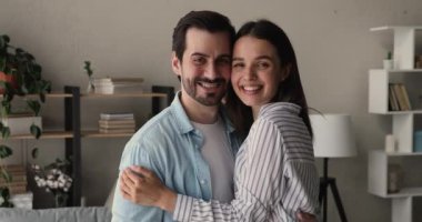 Mutlu çift evde durup kameraya bakarak sarılıyor.