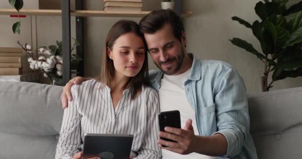 Pareja sentarse en el sofá utilizando aparatos modernos — Vídeo de stock