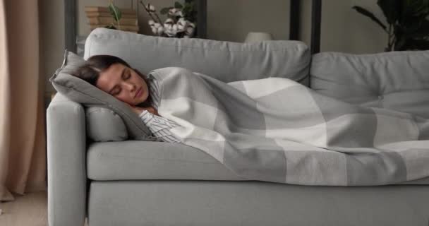 Młoda kobieta leżąca na kanapie cieszyć komfort snu pod kratę — Wideo stockowe
