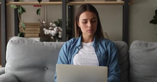 Konzentrierte junge Frau sitzt auf der Couch und arbeitet am Laptop — Stockvideo