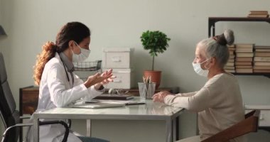 İlgili orta yaşlı kadın ve yüz maskeli genç doktor tedaviyi tartışıyorlar..