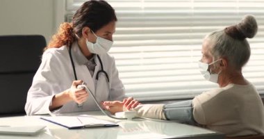 Genç bayan doktor yaşlı kadın hastanın kan basıncını ölçüyor..