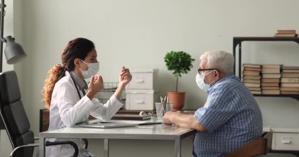 Jeune femme médecin et patient âgé dans des masques de protection communiquant. — Video