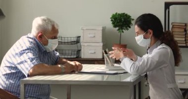 Maskeli genç doktor ve yaşlı hasta ofiste konuşuyor..