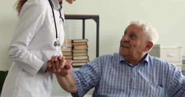 Genç bayan doktor gülümseyen olgun yaşlı adamın elini tutuyor..