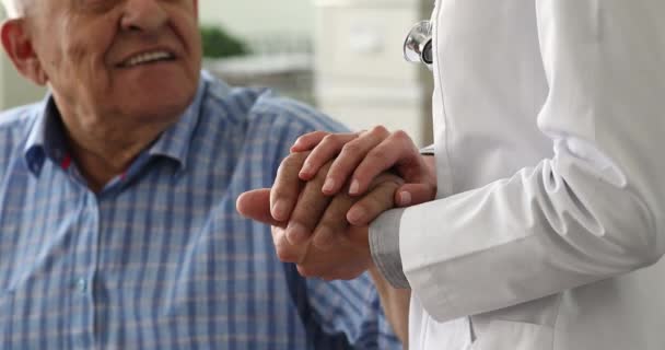 Close up young nurse holding hand of old male patient. — Stock Video