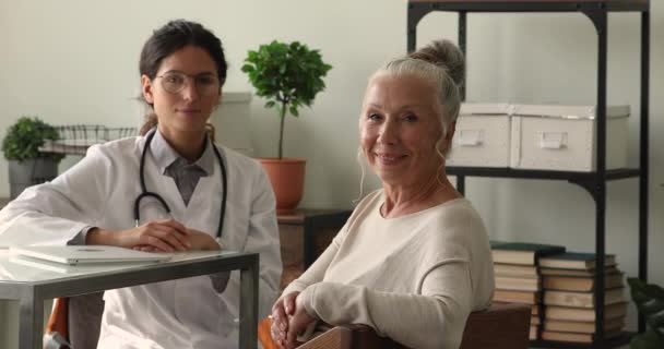 Happy older 60s woman posing with smiling young doctor. — Stock Video