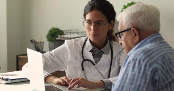 Χαμογελαστός γιατρός που δείχνει τα αποτελέσματα των εξετάσεων στον υπολογιστή στον ηλικιωμένο ασθενή. — Αρχείο Βίντεο