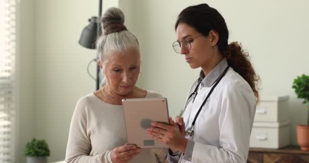 Mujer de 60 años sonriente mirando la pantalla de la tableta con el médico. — Vídeo de stock