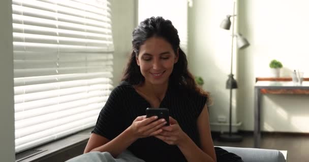 Gülümseyen çekici genç kadın evde cep telefonu kullanıyor.. — Stok video
