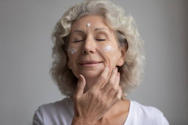 Cilt bakımı gören, gözleri kapalı, rahat, yaşlı bir kadın.
