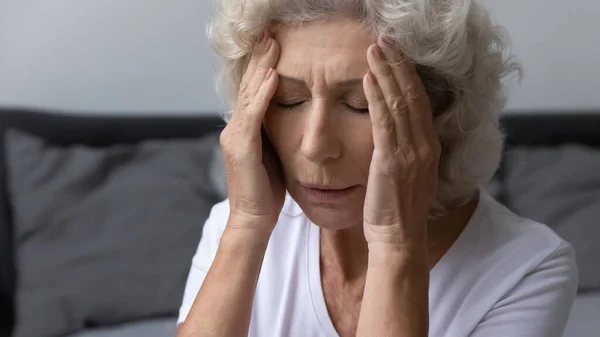 Gefrustreerde, gefrustreerde oudere vrouw die sterke, pijnlijke hoofdpijn heeft — Stockfoto