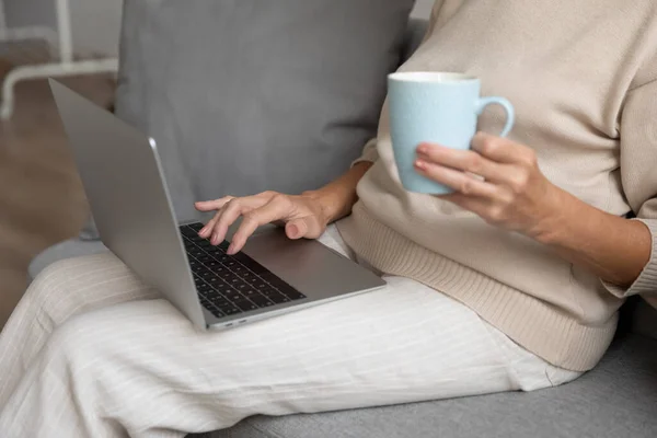 Mature woman using laptop at home, sitting on couch — Stock Photo, Image