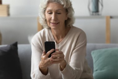 Mutlu yaşlı kadın evden video görüşmesi için akıllı telefon kullanıyor.