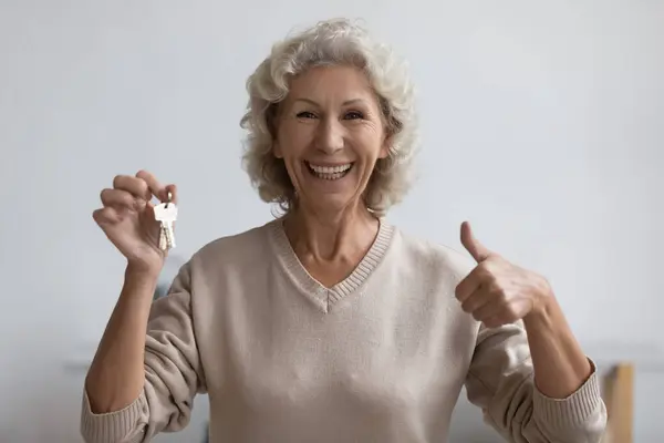 Femme âgée excitée obtenir la clé de la nouvelle maison, montrant comme — Photo