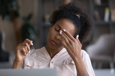 Yorgun çift ırklı kadın iş yerinde baş ağrısı çekiyor.