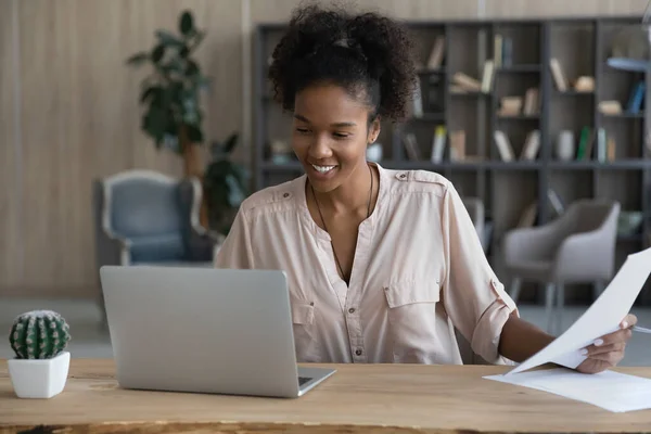 Sonriente mujer afroamericana trabaja en computadora con papeleo —  Fotos de Stock