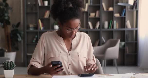 Mujer de etnia africana calculando los gastos domésticos utilizando la aplicación móvil. — Vídeo de stock