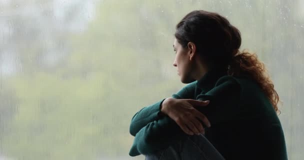 Mujer joven melancólica triste sentado en el alféizar de la ventana, viendo el tiempo lluvioso. — Vídeo de stock