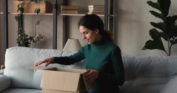 Glimlachende duizendjarige vrouw unboxing kartonnen pakket thuis. — Stockvideo