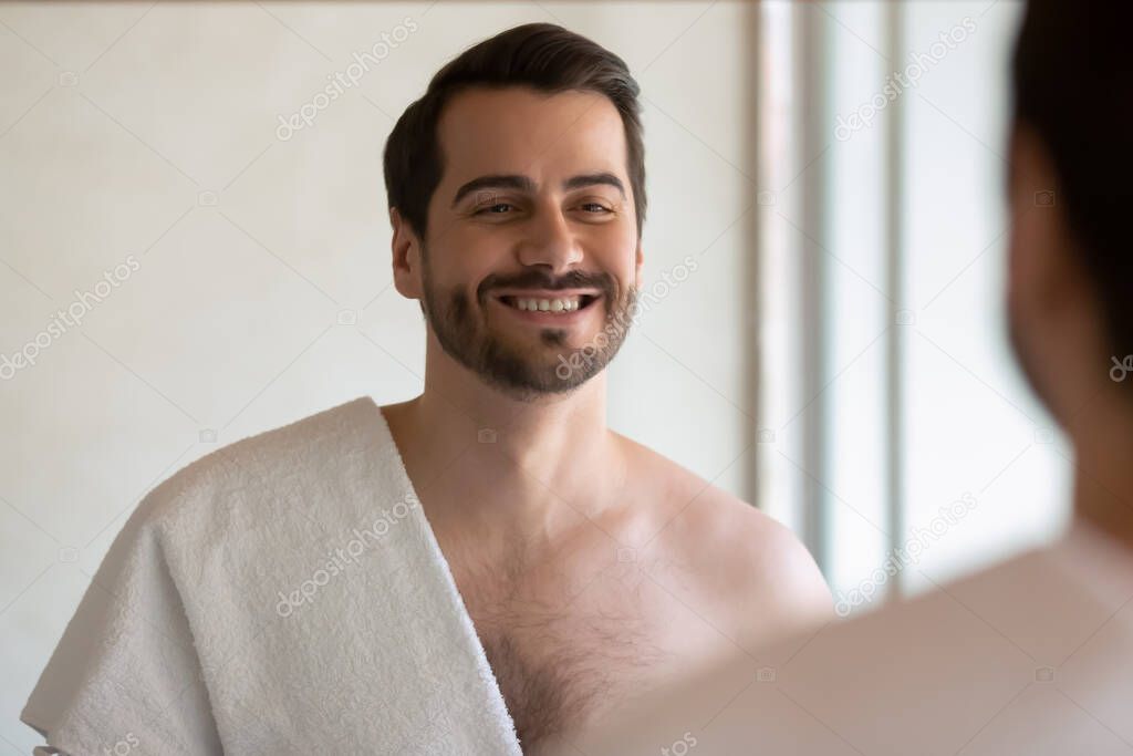 Smiling millennial man look in mirror in bath at home