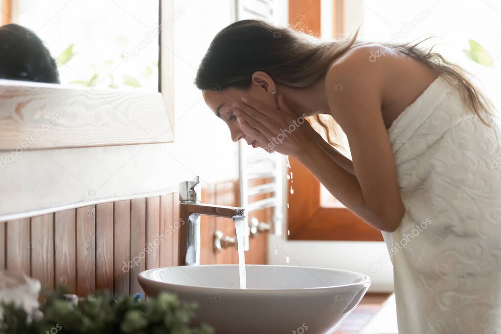 Young woman wash face under running water