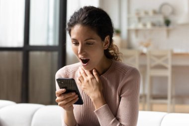 Şaşırmış genç Latin bayan telefon ekranında inanılmaz haberler okuyor.