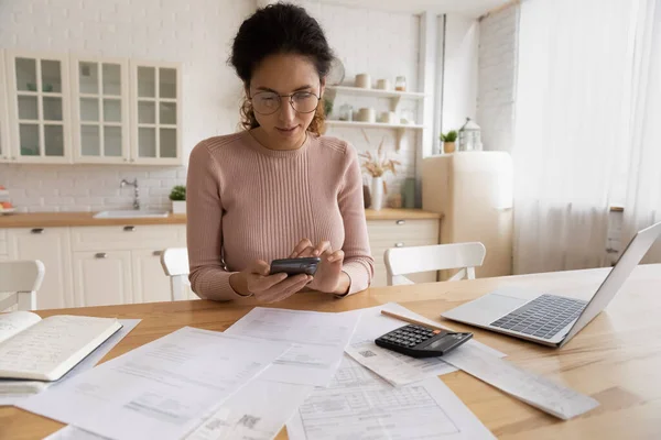 Jonge Spaanse vrouw gebruik moderne telefoon laptop voor thuis boekhouding — Stockfoto