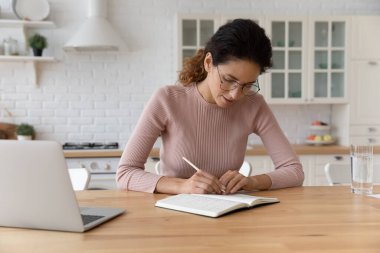 Konsantre olmuş bin yıllık Latin kadın kağıt defterle çalışıyor. Kayıt yapıyor.