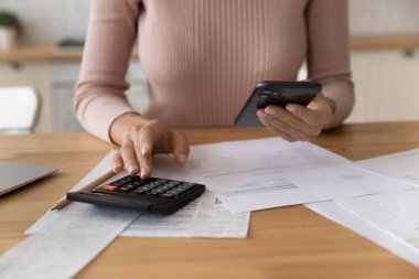 Genç bir kadın mali döküman faturalarını yönetmek için telefon hesap makinesi kullanıyor