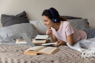 Milenyum dişisi kulaklık takıyor ve diz üstü bilgisayar kullanıyor.