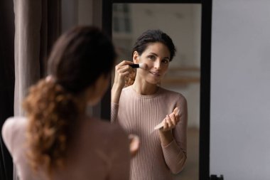 Büyüleyici Latin kadın aynaya bak fırça kullan pudra sür