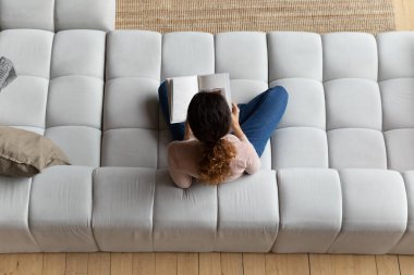 Genç bayan kanepede oturup boş sayfalarla kitap okuyor.