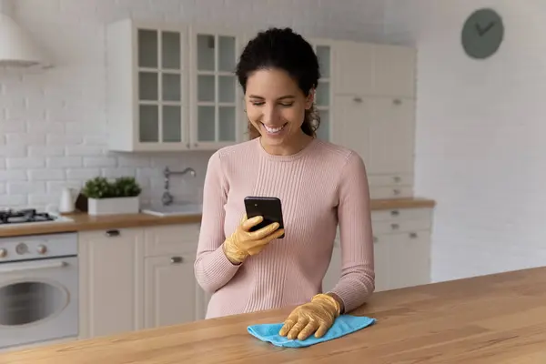 Mutlu genç İspanyol kadın mutfağı parlatır ve akıllı telefon uygulaması kullanır. — Stok fotoğraf