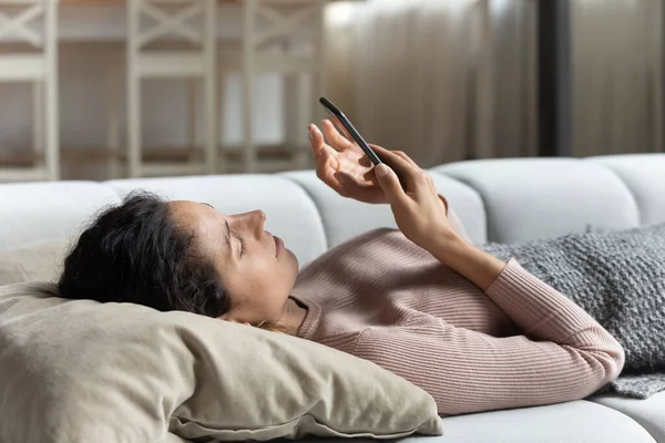 Perezosa joven descanso en el sofá después de despertarse con el teléfono celular — Foto de Stock