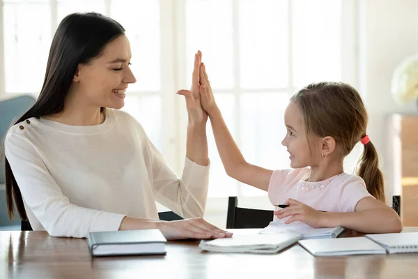 Feliz mamá y la pequeña hija terminan los deberes dan cinco altos —  Fotos de Stock