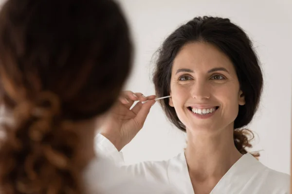 Reflexão do espelho da mulher sorridente limpando orelhas, usando o botão de algodão — Fotografia de Stock