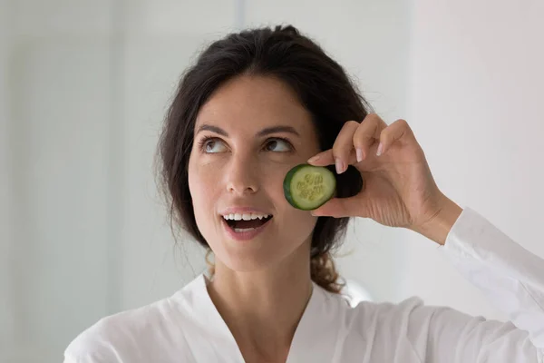Close up gelukkig mooi vrouw holding komkommer slice, huidverzorging routine — Stockfoto