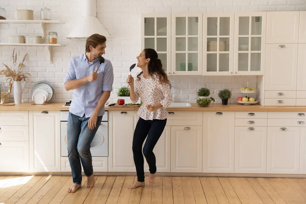 Overjoyed young couple singing into kitchenware, dancing in kitchen — Stock Photo, Image