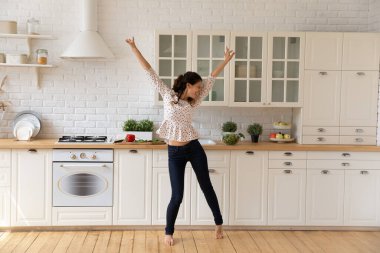 Neşeli genç bir kadın dans ediyor, modern bir mutfağa atlıyor.