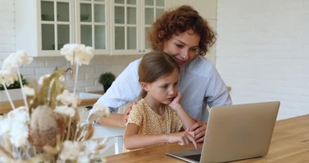 Mujer ayuda a la hija con el trabajo escolar utilizando el ordenador portátil en casa — Vídeos de Stock