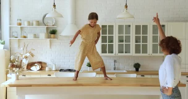 Дівчина виконує танці на обідньому столі, розважаючись з мамою — стокове відео
