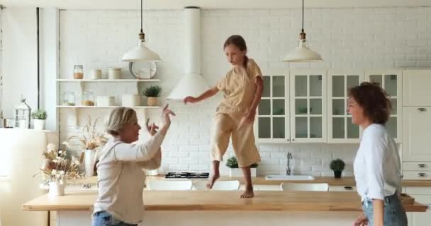 Chica bailando en la mesa divirtiéndose con mamá y abuela — Vídeo de stock