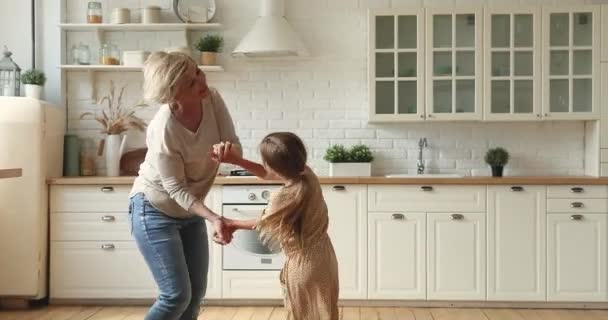 Liten flicka dansar med äldre mormor i köket — Stockvideo