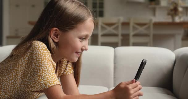 女の子はソファの上に横たわっている携帯電話を使用してインターネット上で楽しい — ストック動画