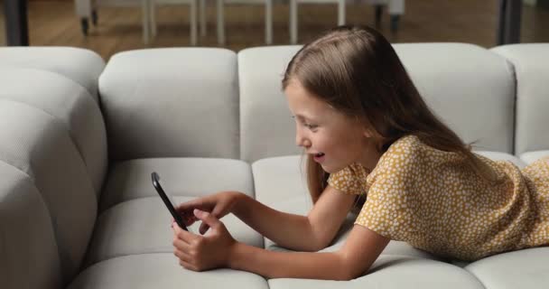 Menina deitada no sofá segurando smartphone desfrutar de aplicativos on-line — Vídeo de Stock