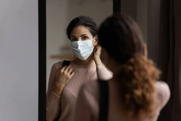 Young latina lady look at mirror in protective medical mask