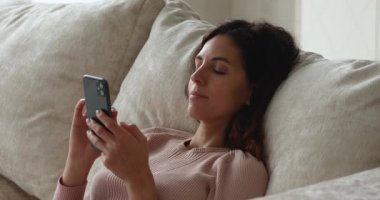 Bekar, rahat bir kadın kanepe yastıklarında yatarken akıllı telefon kullanır.