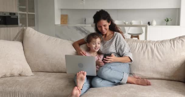 Madre e hija relajarse en el sofá con el ordenador portátil y el teléfono inteligente — Vídeo de stock