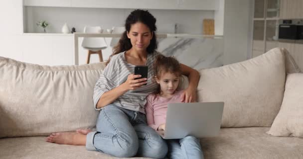 Mulher em seu telefone enquanto pequena filha joga no laptop — Vídeo de Stock